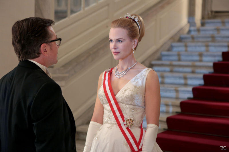 Eine Frau in einem weißen Kleid mit Diadem und ein Mann im schwarzen Anzug stehen vor einer Treppe.