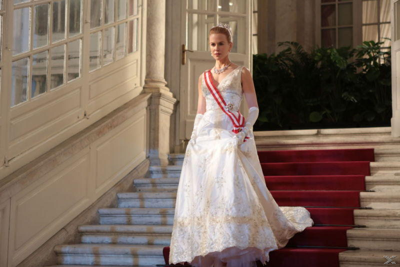Eine Frau in einem weißen Kleid und Diadem steht auf einer Treppe mit rotem Teppich.