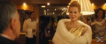 Eine Frau in einem goldenen Kleid und einem weißen Pelzmantel steht in einem Raum.