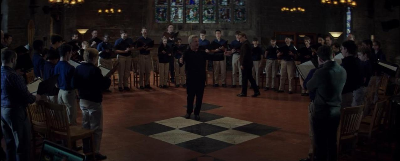 Ein Chorleiter dirigiert eine Gruppe von Jungen in einer Kirche mit Buntglasfenstern.