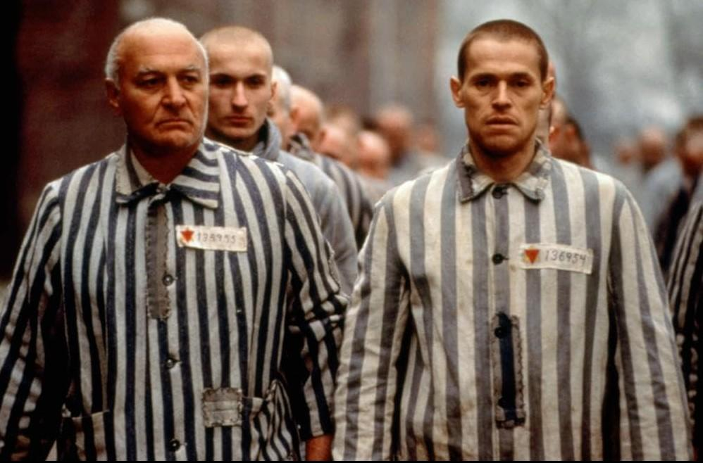 Männer in gestreiften Gefängnisuniformen marschieren in einer Reihe, mit Nummern auf ihren Hemden.