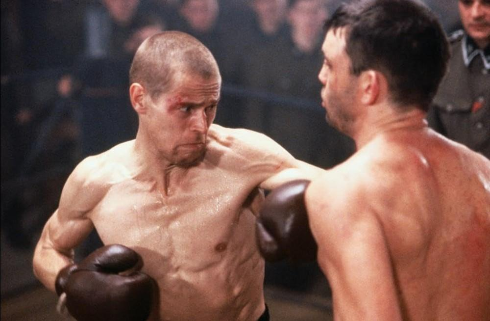 Zwei Boxer im Ring mit dunklen Handschuhen kämpfen. Einer hat eine Wunde im Gesicht.