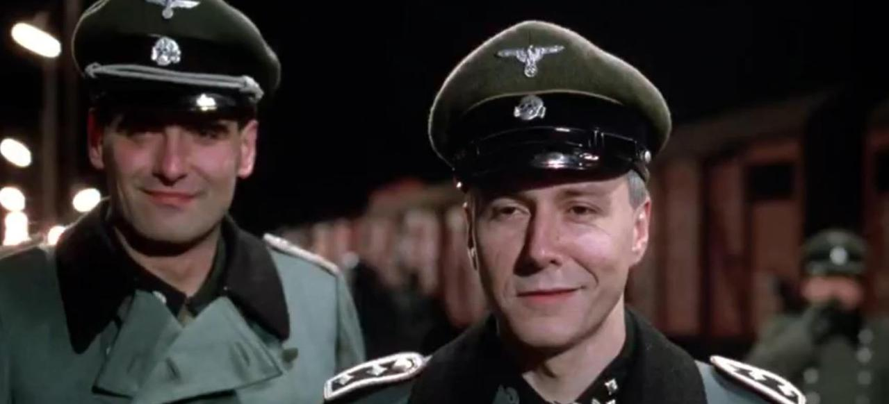 Zwei Männer in Uniformen mit Hüten und Mänteln lächeln.