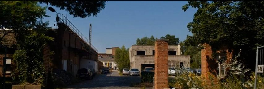 Industrieller Hof mit Autos und alten Gebäuden unter blauem Himmel.