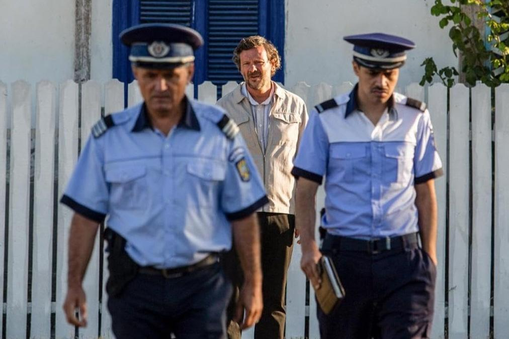 Zwei Polizisten in Uniform und ein Mann gehen auf eine weiße Holzzaun zu.