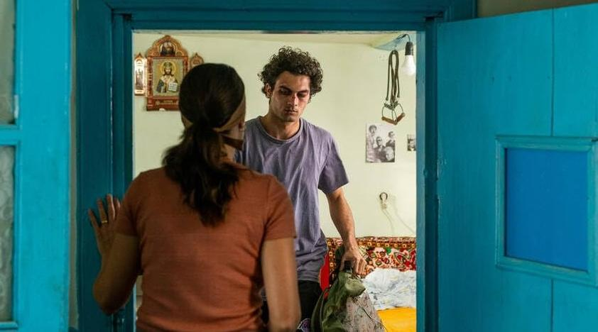 Mann mit dunklen Locken und Frau stehen in einem Raum mit blauen Türen.