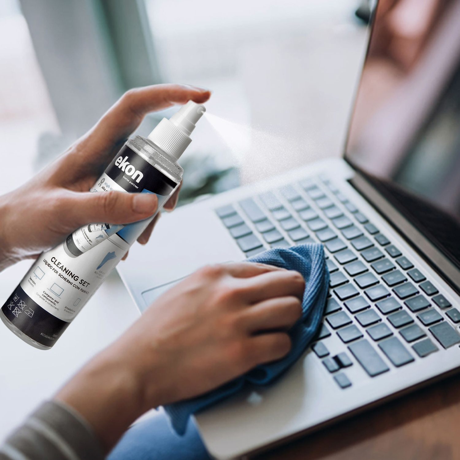 Una mano spruzza liquido detergente su una tastiera del laptop, un'altra la pulisce.