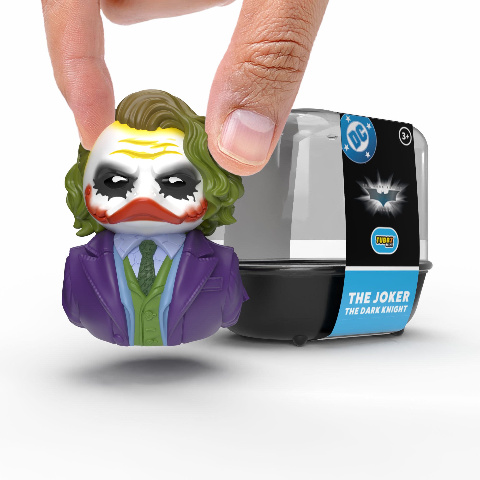 Egy ujj egy lila öltönyös mini Joker figurát tart egy fekete csomagolás mellett.