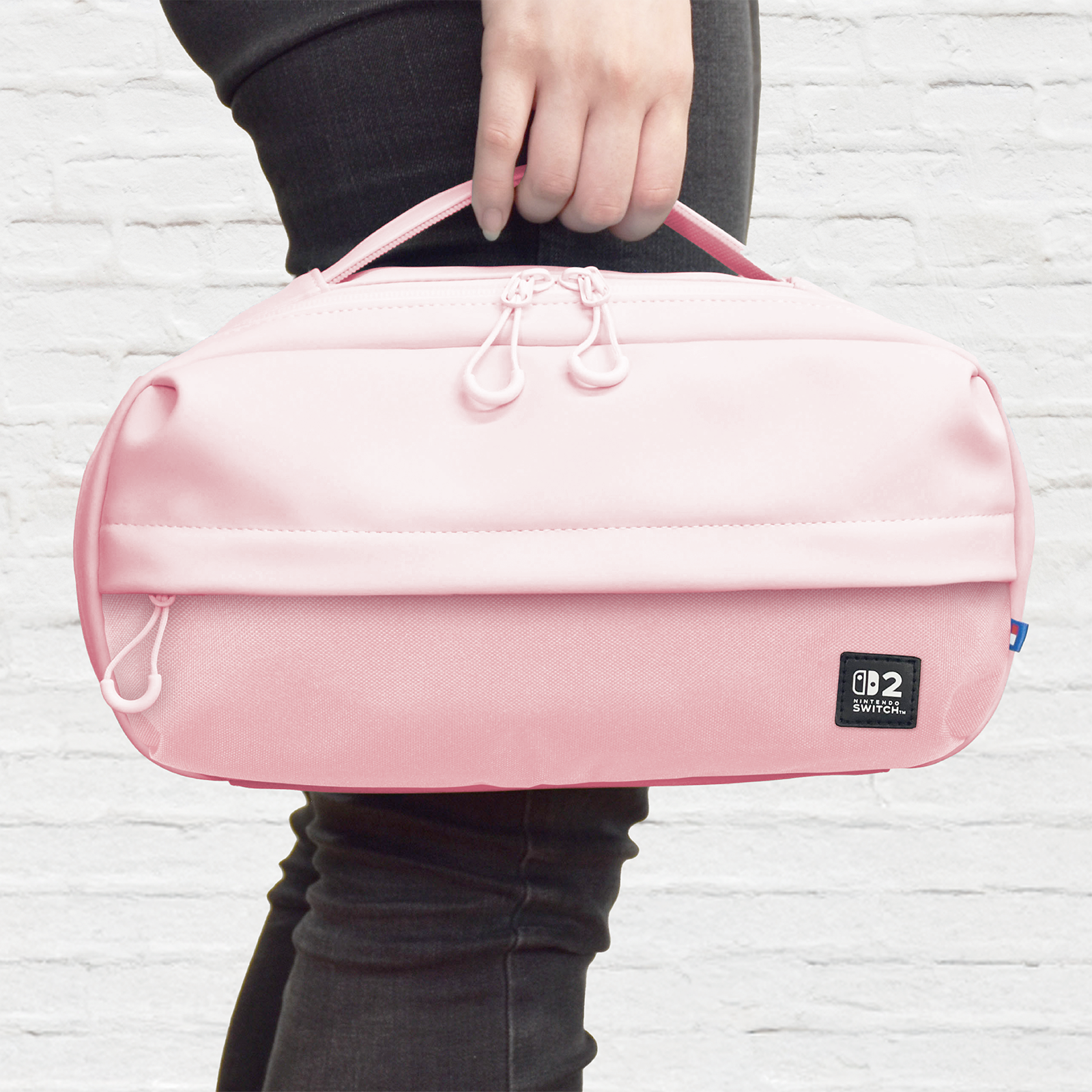 Eine Person hält eine rosafarbene Nintendo Switch Tasche mit zwei Reißverschlüssen und Nintendo Switch Logo.