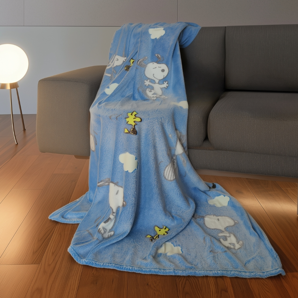Eine blaue Decke mit Snoopy und Woodstock-Motiv liegt auf einem Sofa.