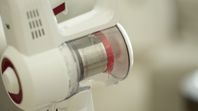 Gros plan d'un aspirateur sans fil blanc avec des touches rouges et un collecteur de poussière transparent.