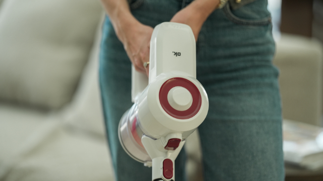 Une personne en jean tient un aspirateur à main blanc avec des accents rouges.