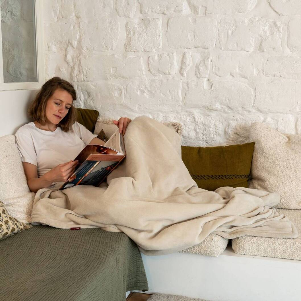 Una donna legge un libro, avvolta in una coperta, seduta su un divano.