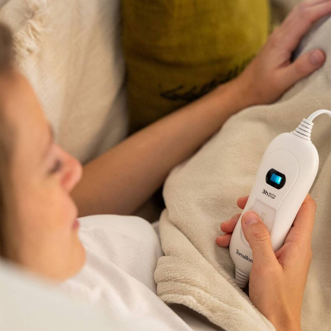 Una donna tiene un telecomando bianco con luce blu su una coperta.