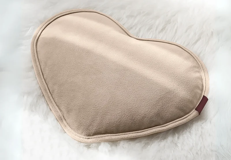 Une bouillotte beige en forme de cœur repose sur un tapis blanc et moelleux.