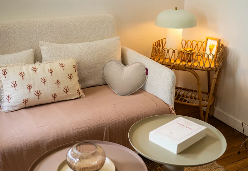 Un coussin beige en forme de cœur sur un jeté rose sur un canapé crème.