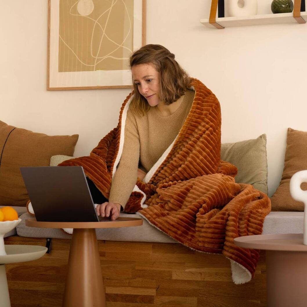 Donna con laptop sotto coperta su divano.