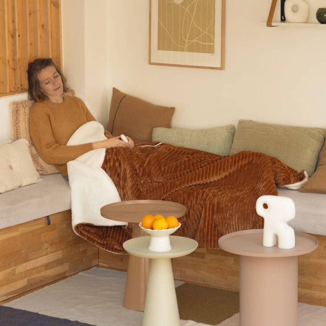 Una donna si rilassa sotto una coperta su un divano, con arance su un tavolino vicino.