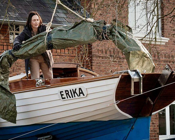 Eine Frau zieht ein grünes Verdeck über ein Boot mit dem Namen Erika.