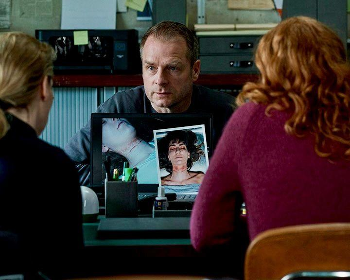 Drei Personen betrachten Fotos von Leichen auf einem Laptop.