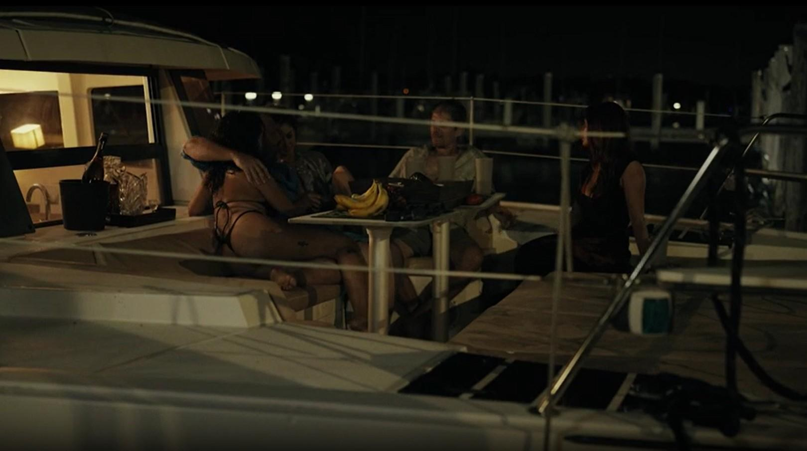 Menschen auf einer Yacht bei Nacht, mit Früchten auf einem Tisch.