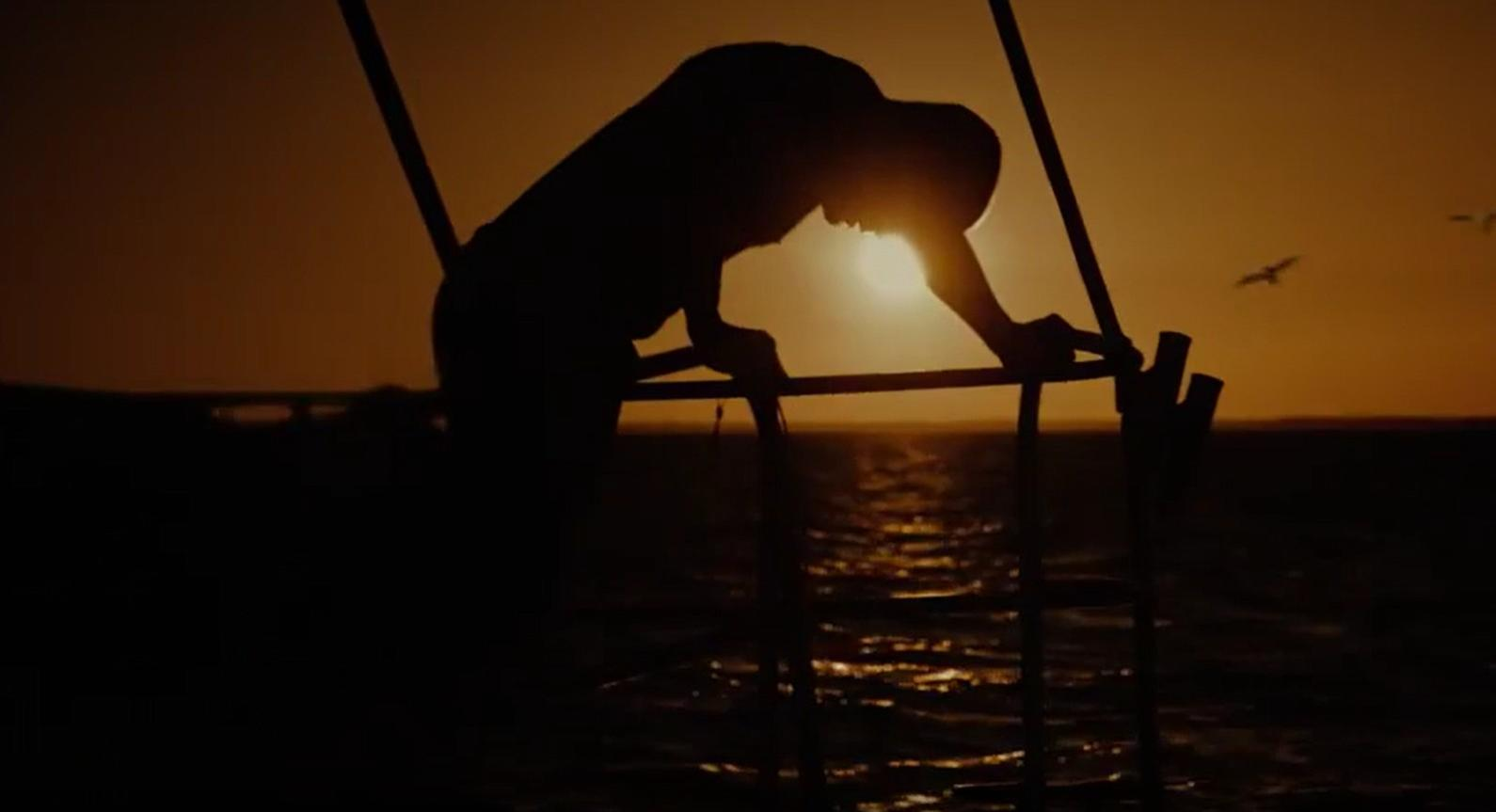 Silhouette eines Mannes auf einem Boot bei Sonnenuntergang über dem Meer.