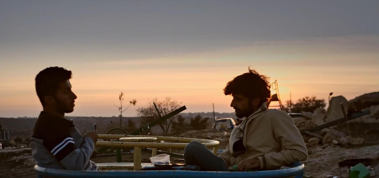 Zwei Männer sitzen auf einem Karussell bei Sonnenuntergang.
