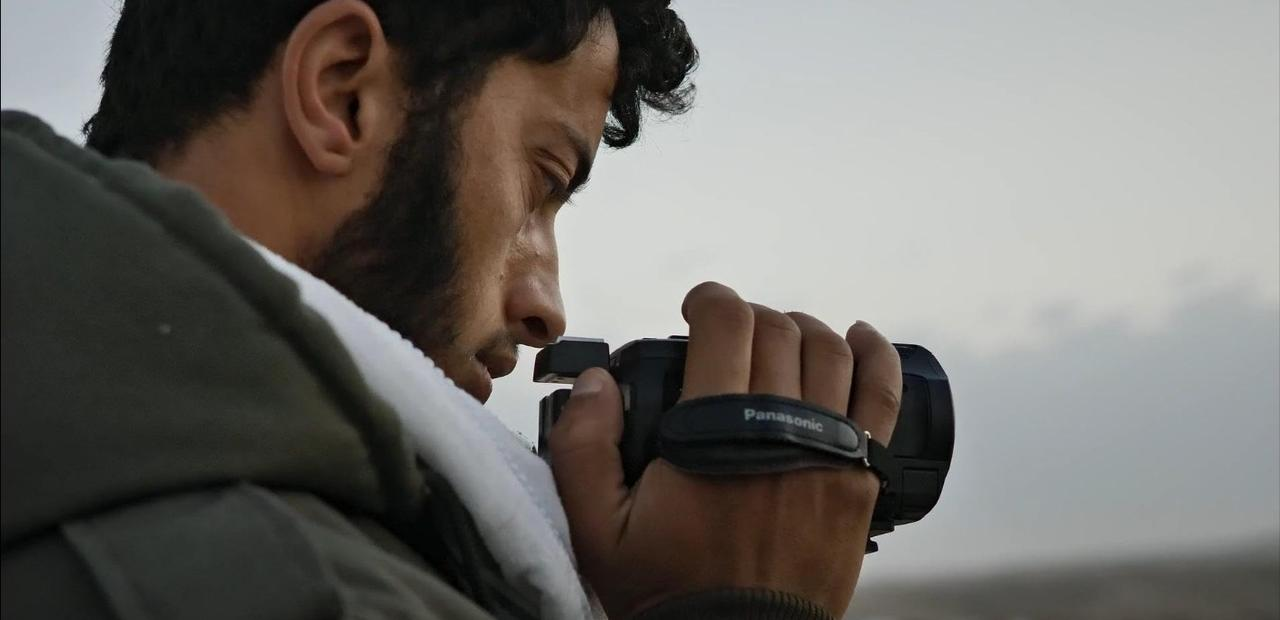 Mann filmt mit Camcorder, Nahaufnahme, bewölkter Himmel im Hintergrund.