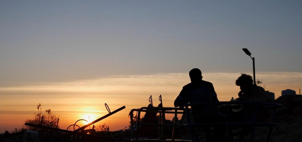 Silhouette von zwei Personen auf einem Spielplatz bei Sonnenuntergang.