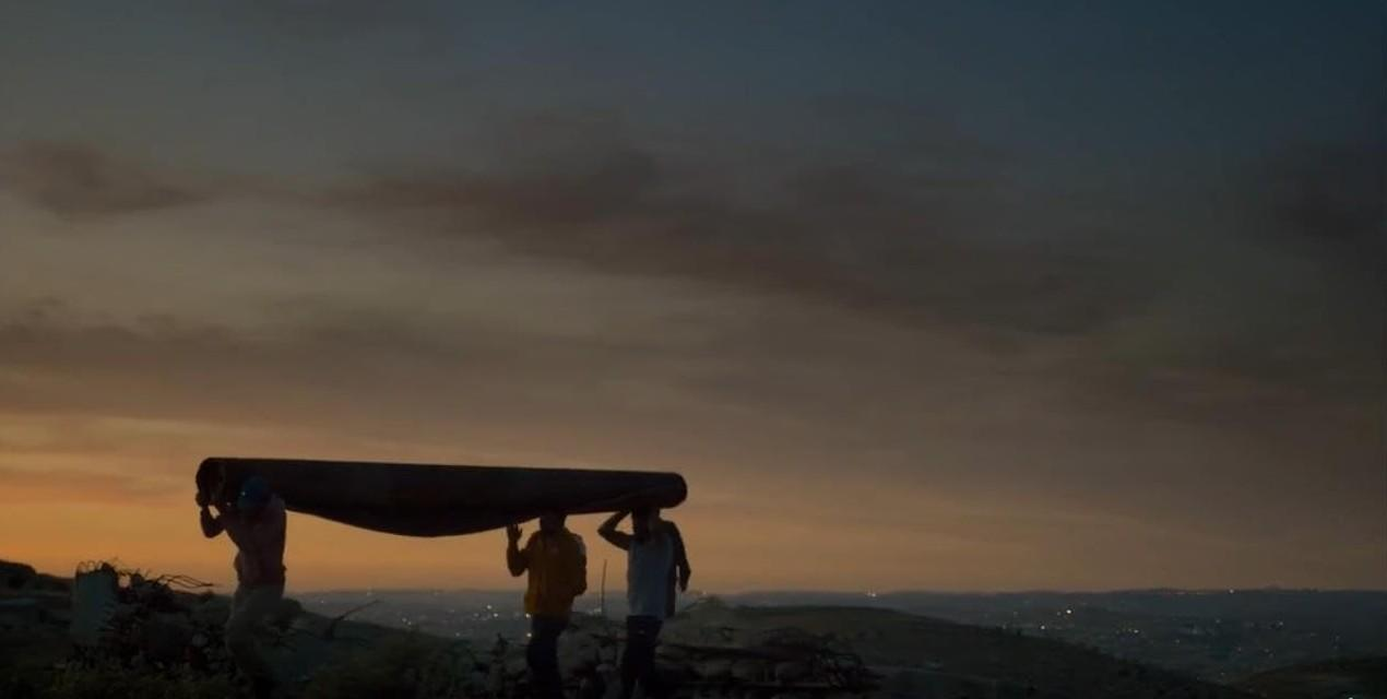 Drei Männer tragen eine lange Rolle auf einem Hügel bei Sonnenuntergang.