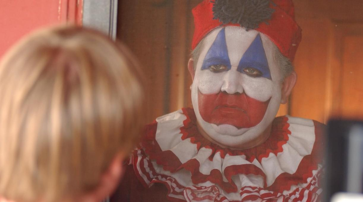 Ein Mann mit Clown-Make-up und einer roten Kappe blickt durch ein Netz.