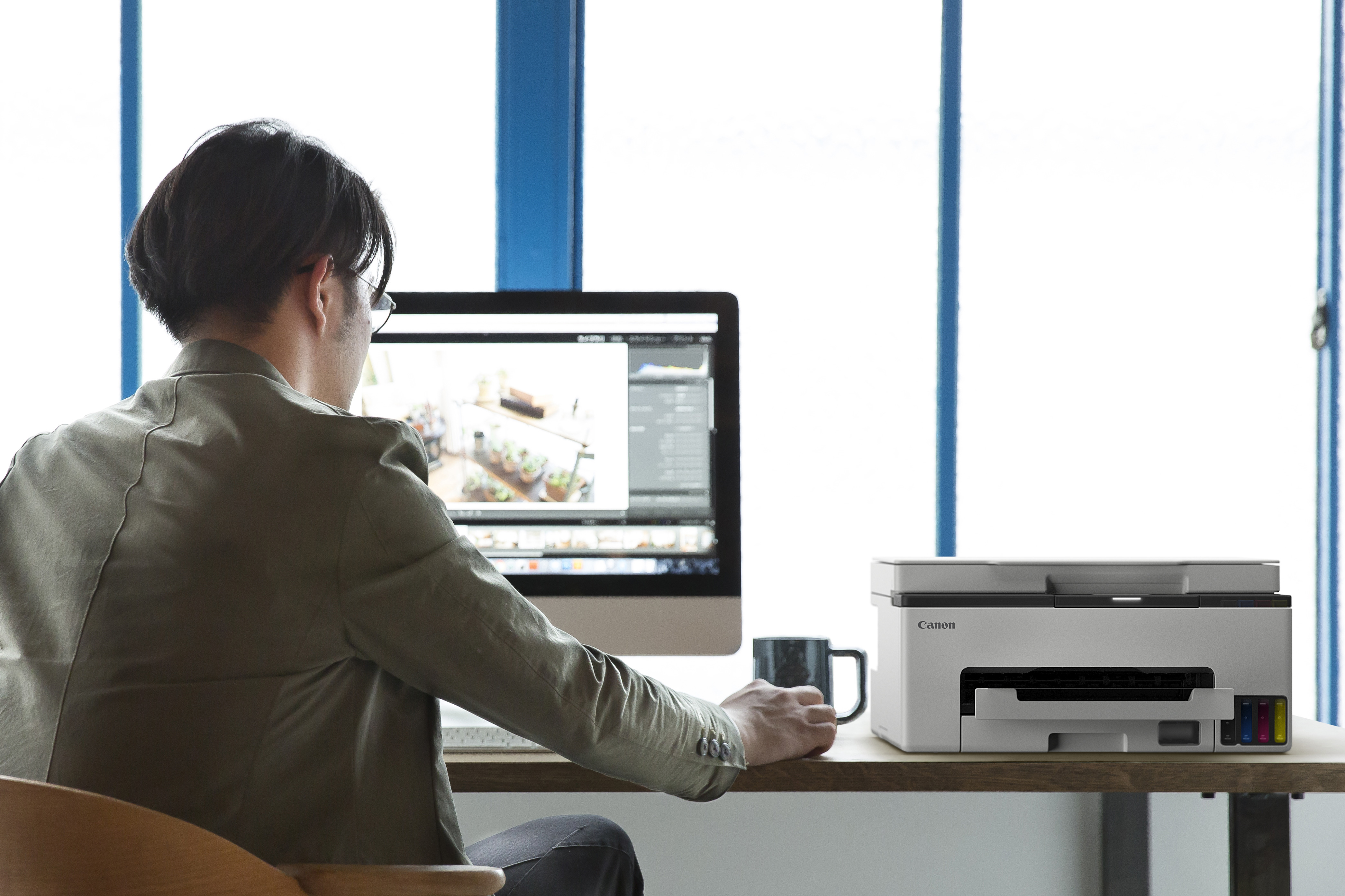 Mann sitzt am Schreibtisch, Canon Drucker, Computerbildschirm mit Pflanzenbild.