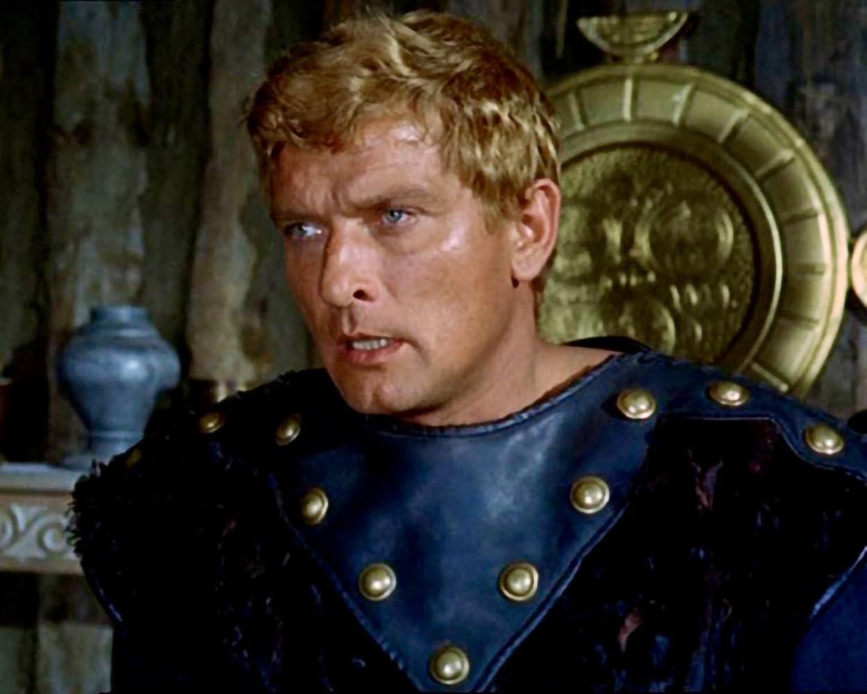 Ein Mann mit blonden Haaren trägt eine dunkle Rüstung mit goldenen Nieten.
