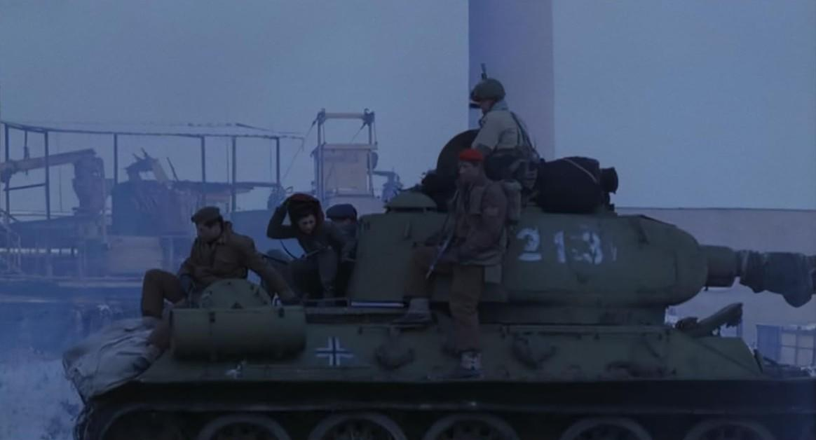 Soldaten auf einem Panzer vor industrieller Kulisse bei Dämmerung.