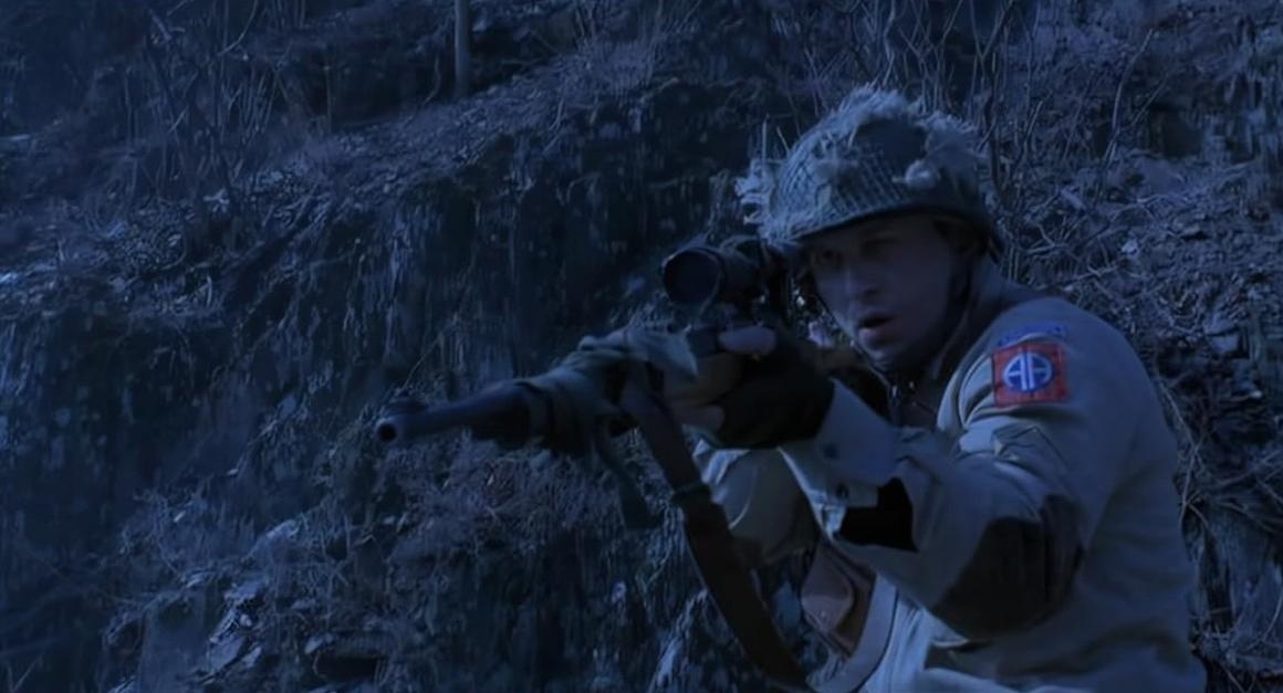 Ein Soldat im Tarnanzug zielt mit einem Gewehr auf felsigem Gelände.