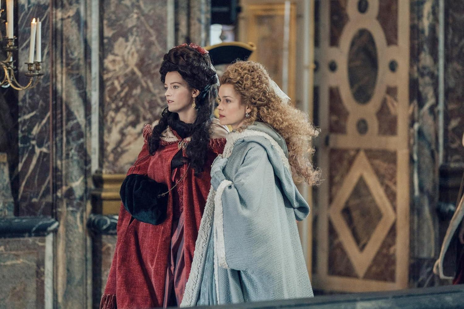 Zwei Frauen in historischen Kostümen stehen nebeneinander in einem opulenten Raum.