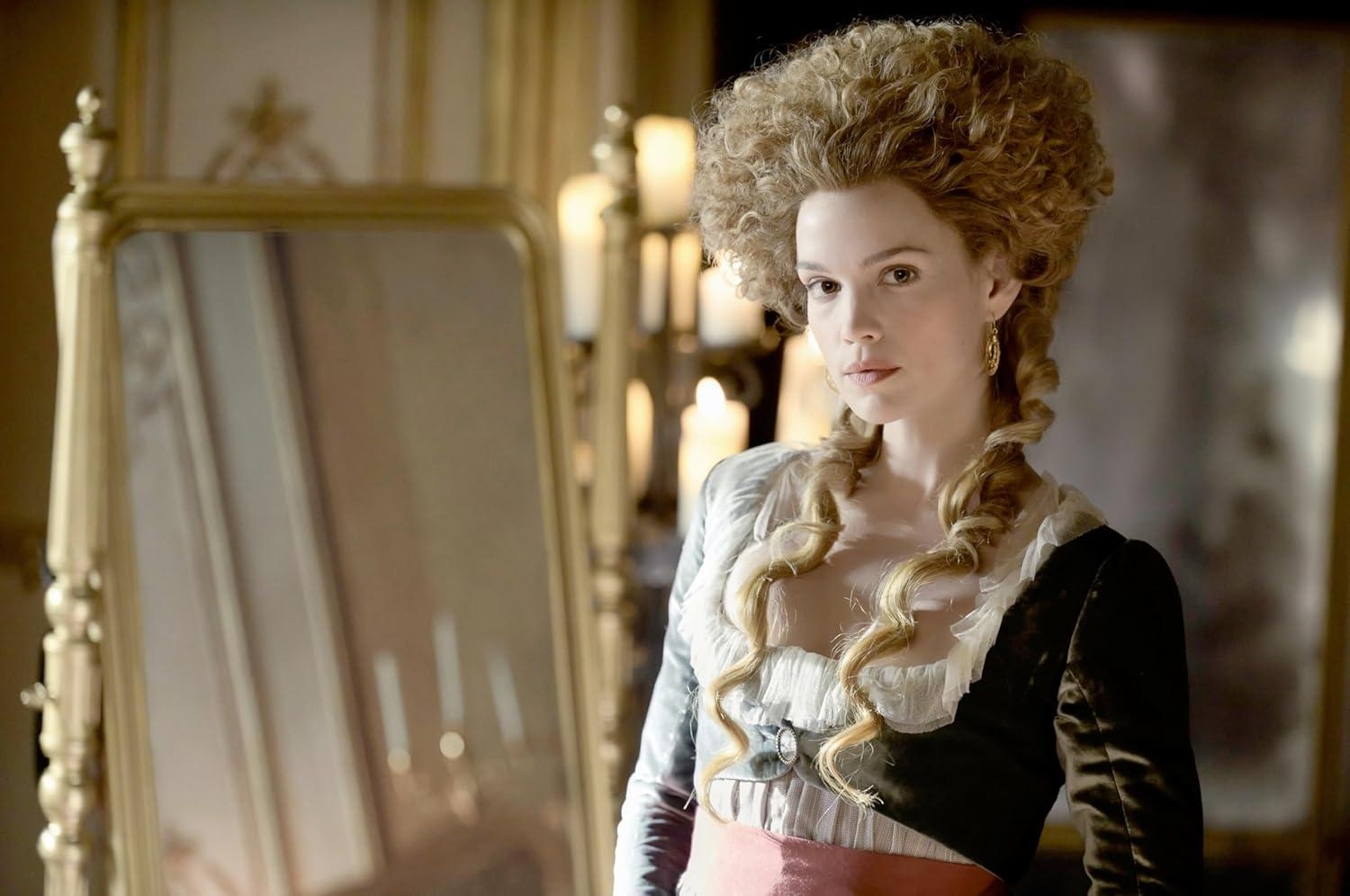 Eine Frau mit aufwendiger Frisur und historischem Kleid steht vor einem Spiegel.