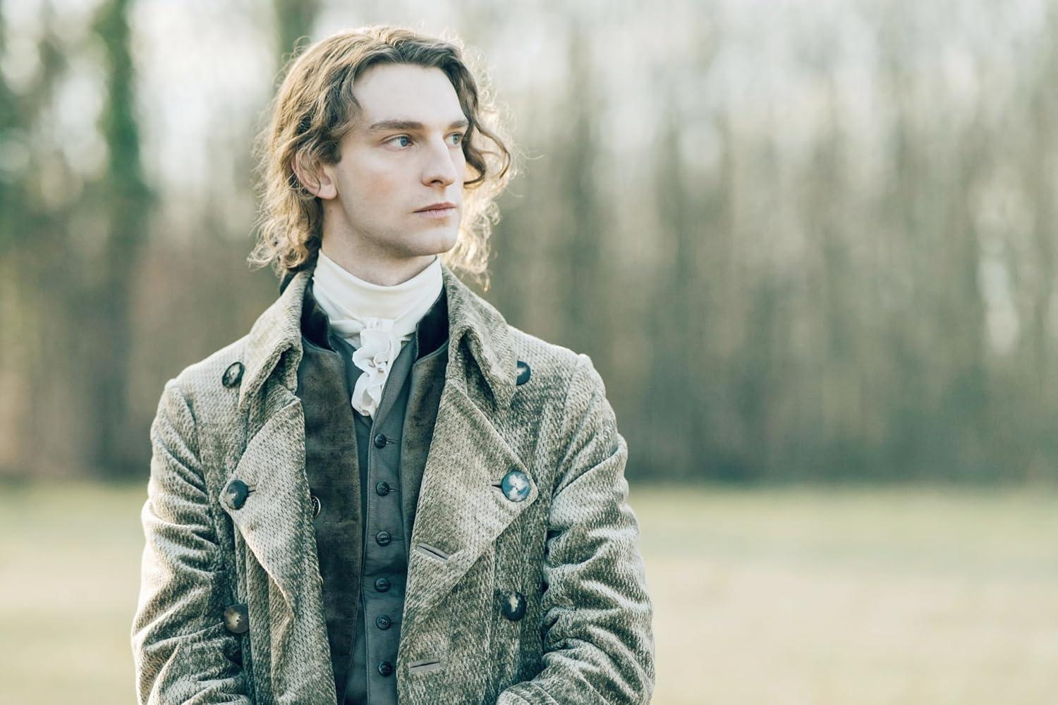 Ein Mann mit langen Haaren in historischer Kleidung steht im Freien.