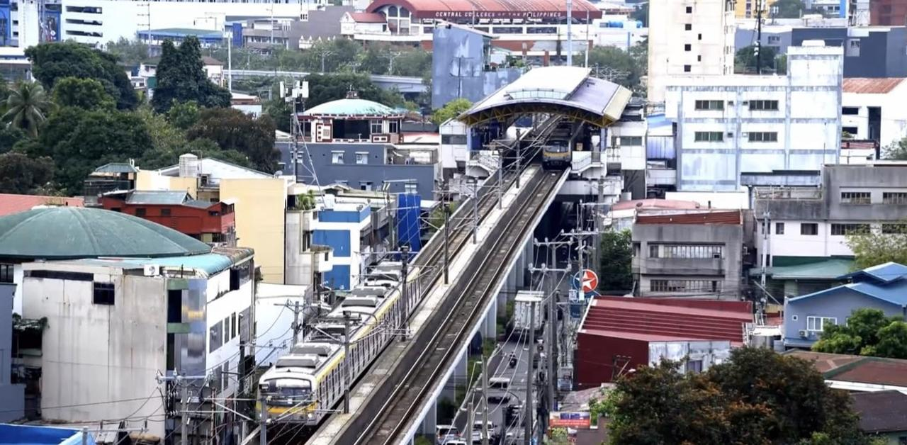 Ein Zug fährt auf erhöhten Schienen über eine Stadt mit Gebäuden und Bäumen.