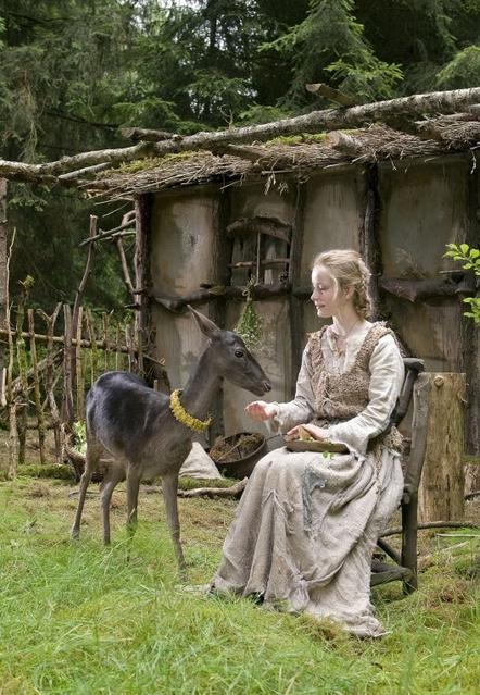 Frau in rustikalem Outfit füttert Reh mit gelbem Halsband in einem Wald.