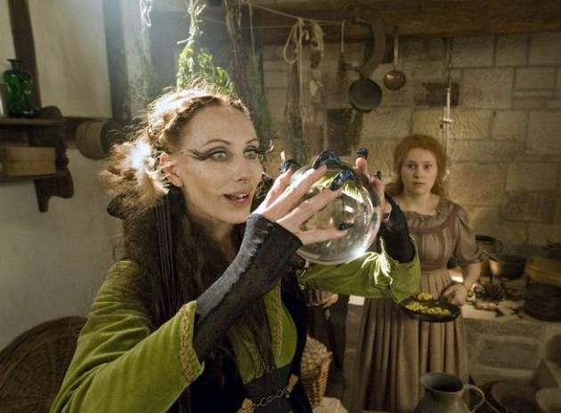 Eine Frau mit langen Wimpern hält eine Kristallkugel. Eine andere Frau steht im Hintergrund.