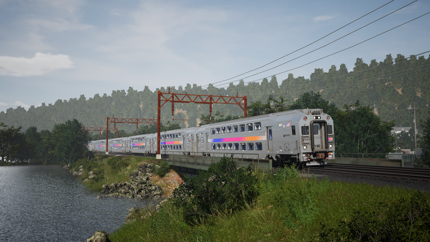 Un tren plateado cruza un puente junto a un río, bordeado de árboles.