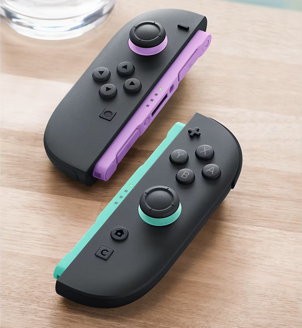 Zwei Controller liegen auf einem Holztisch, einer violett, der andere mintgrün.