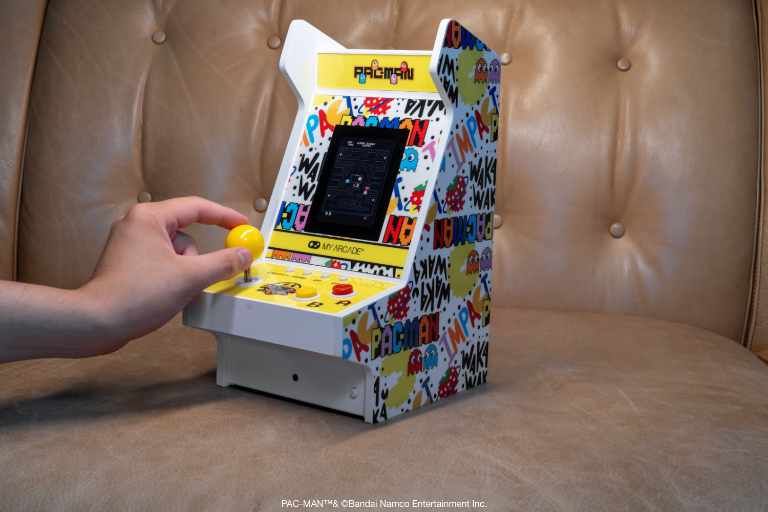 Kahverengi deri koltukta mini Pac-Man arcade makinesinin joystick'ini bir el kumanda ediyor.