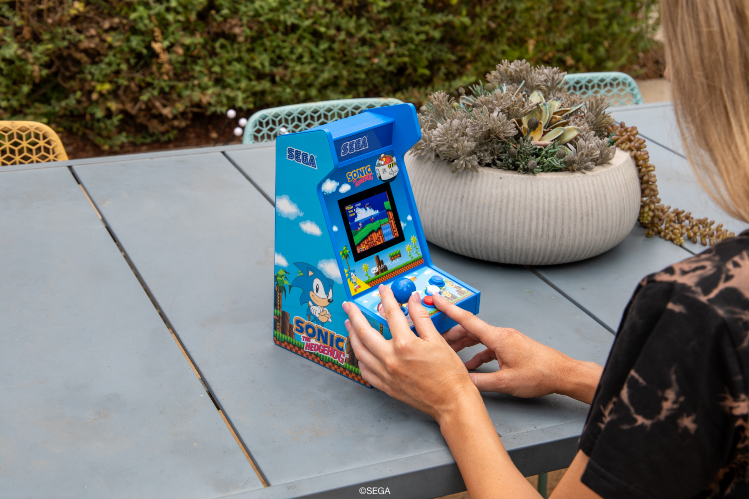 Bir kişi dışarıda mavi Sonic the Hedgehog arcade konsolu oynuyor.