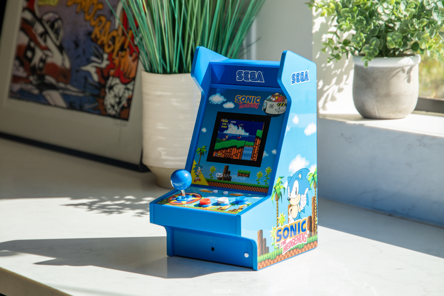 Mermer yüzeyde duran küçük mavi bir Sonic the Hedgehog arcade oyun makinesi.