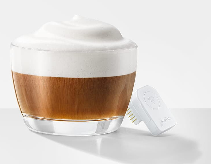 Szklanka kawy z pianką mleczną i biała wtyczka z pinami.