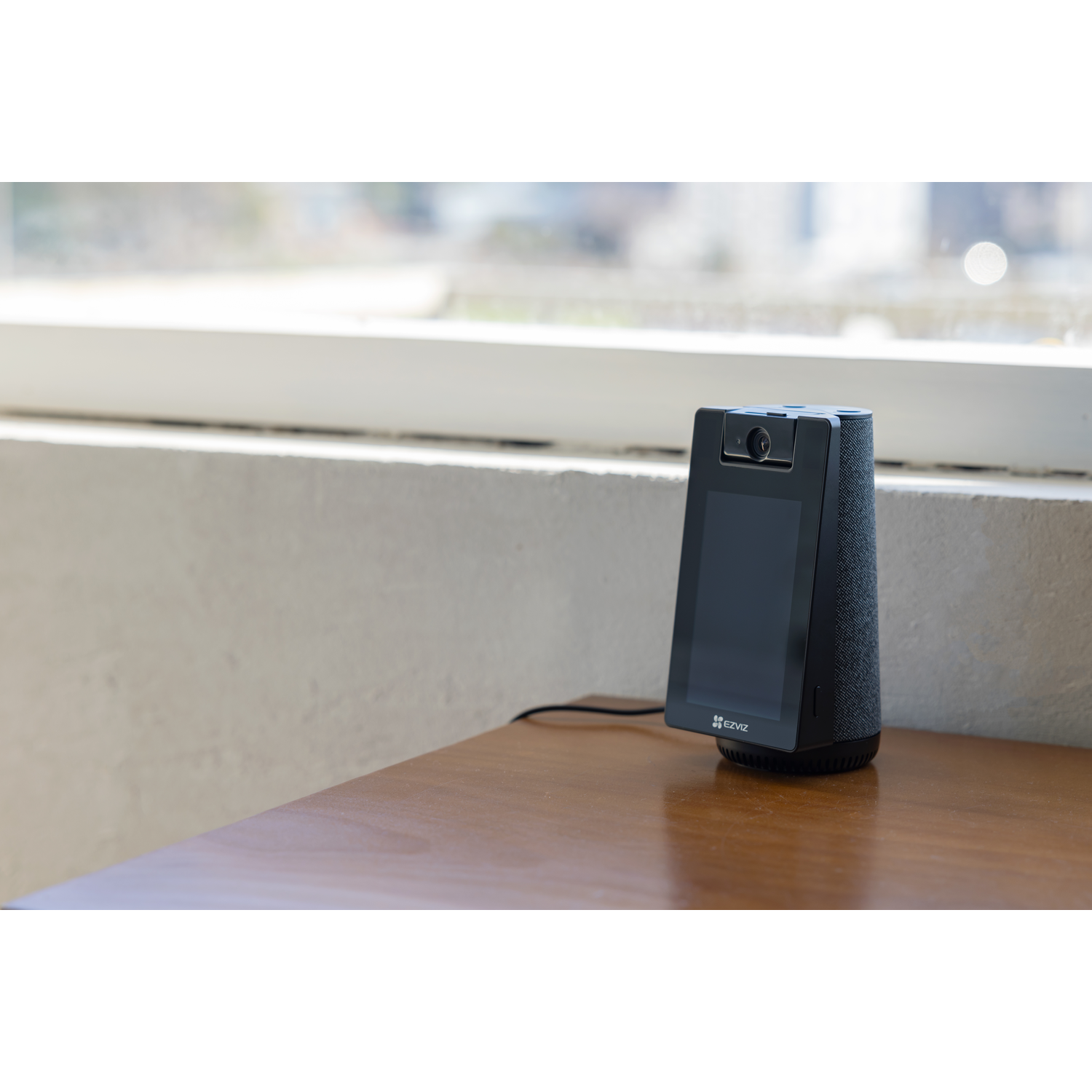 A black smart speaker with a screen and camera sits on a wooden table.