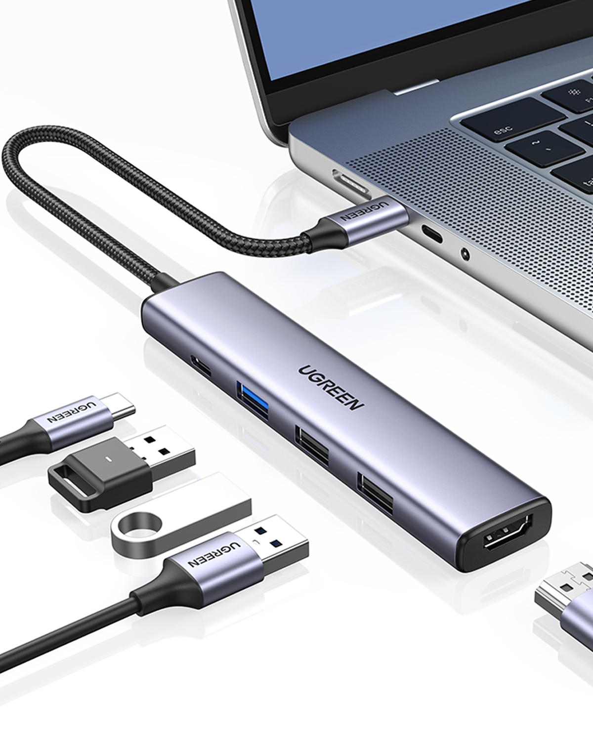 Portları olan gri USB-C hub bir dizüstü bilgisayara bağlı, yanında USB bellekler.