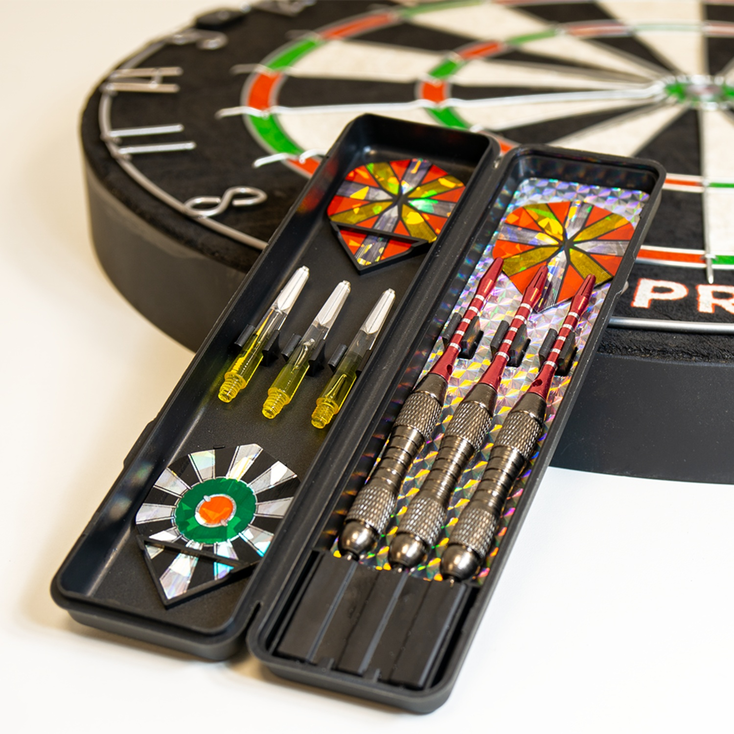 A dartboard and a case with darts. Three red darts and three yellow darts are visible.